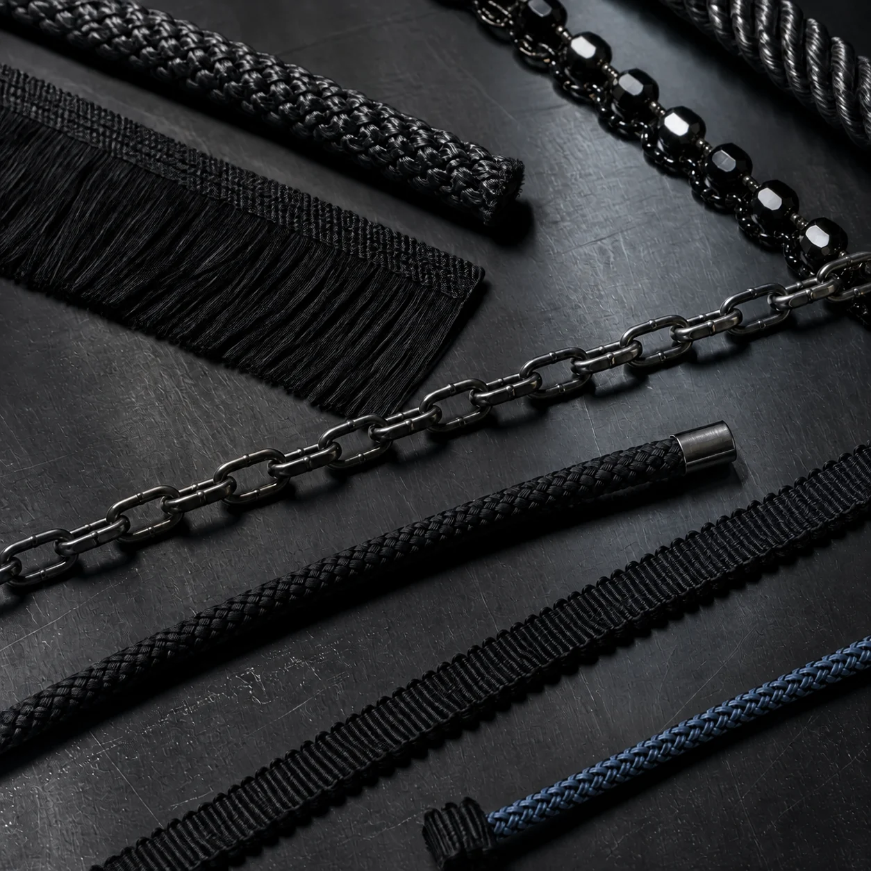 Fashion decorative cords, braided trims and metal chain details arranged in a dark material study